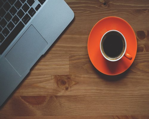 A professional workspace with a standard laptop computer and an espresso cup near it